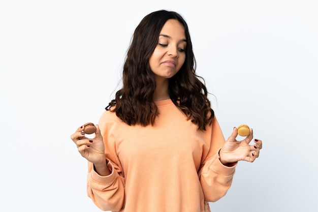 Mujer joven sobre fondo blanco aislado sosteniendo coloridos macarons franceses y mirándolo