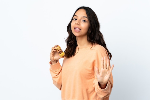 Mujer joven sobre fondo blanco aislado sosteniendo coloridos macarons franceses y saludando