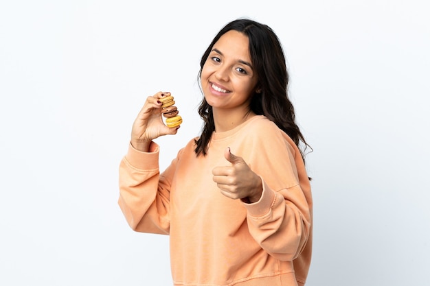 Mujer joven sobre fondo blanco aislado sosteniendo coloridos macarons franceses con Thumbs up