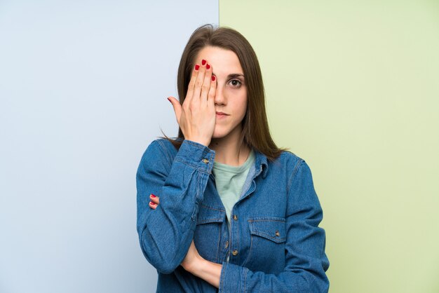 Mujer joven sobre el fondo colorido que cubre un ojo a mano