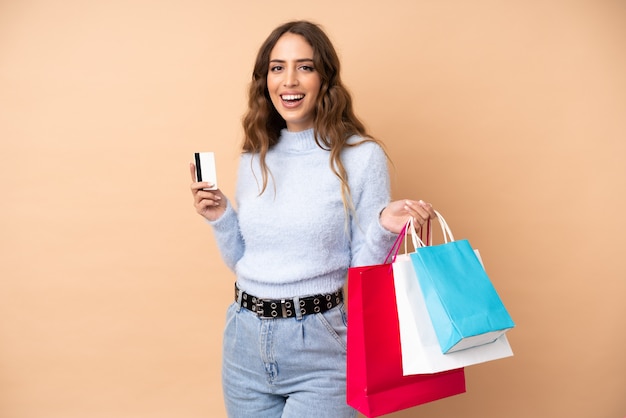 Mujer joven sobre pared aislada con bolsas de compras y una tarjeta de crédito