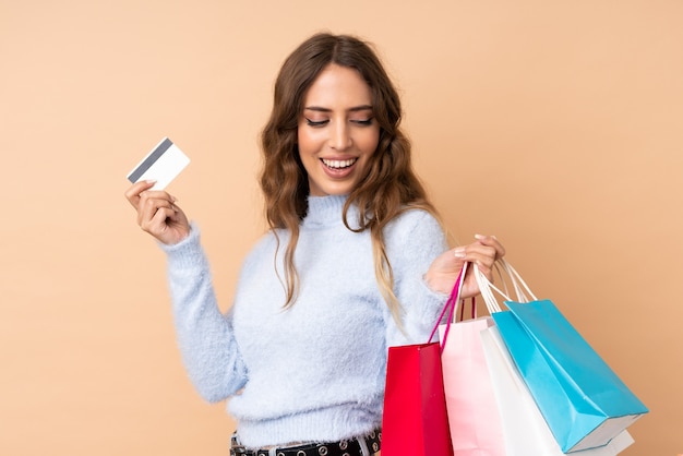 Mujer joven sobre pared aislada con bolsas de compras y una tarjeta de crédito