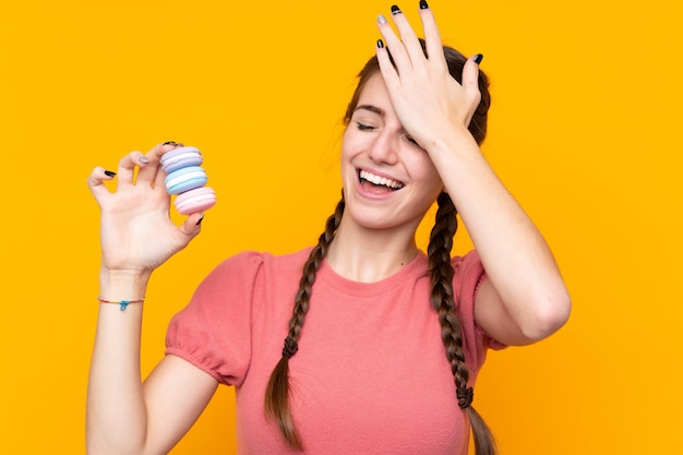 Mujer joven sobre pared amarilla aislada con coloridos macarons franceses y con la intención de la solución