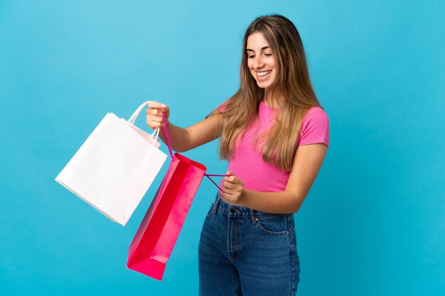 Mujer joven sobre pared azul aislada con bolsas de compras