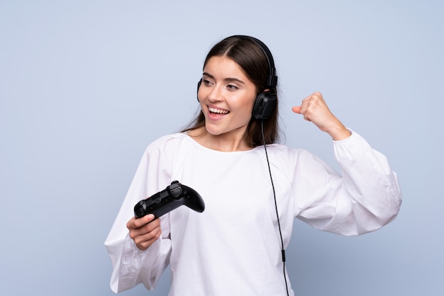 Mujer joven sobre pared azul aislada jugando en videojuegos