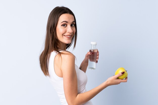 Mujer joven sobre pared azul aislada con una manzana y con una botella de agua