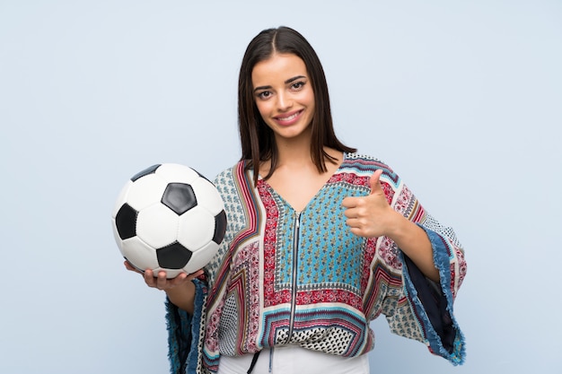 Mujer joven sobre pared azul aislada sosteniendo un balón de fútbol