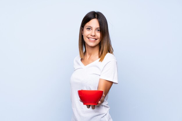 Mujer joven sobre pared azul aislada sosteniendo un tazón de cereales