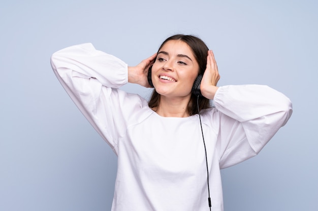 Mujer joven sobre pared azul aislada usando el móvil con auriculares