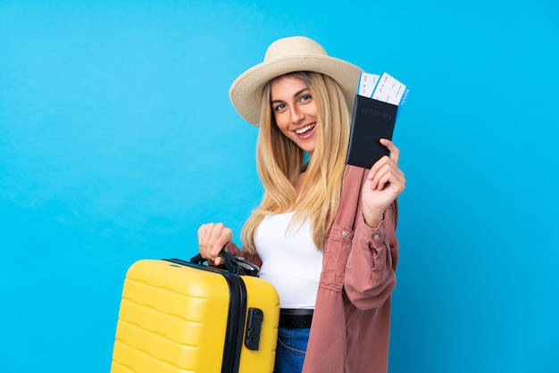 Mujer joven sobre pared azul aislada en vacaciones con maleta y pasaporte