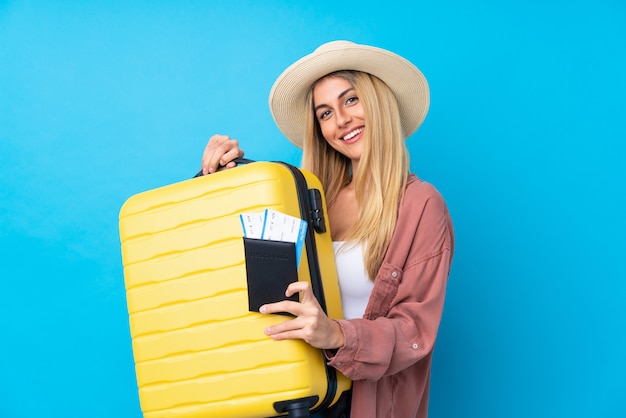 Mujer joven sobre pared azul aislada en vacaciones con maleta y pasaporte