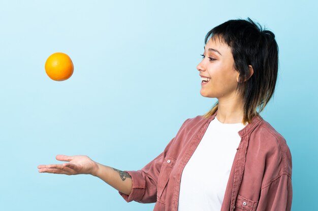 Mujer joven sobre pared azul con una naranja