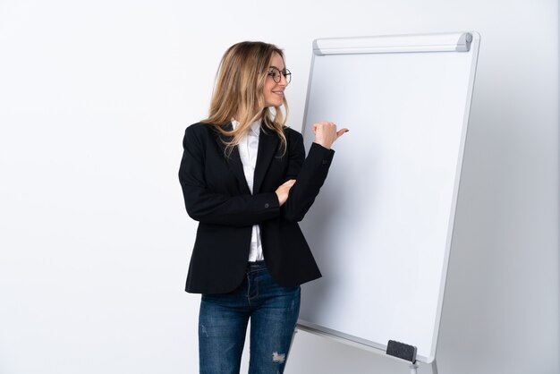 Mujer joven sobre pared blanca aislada apuntando hacia un lado para presentar un producto