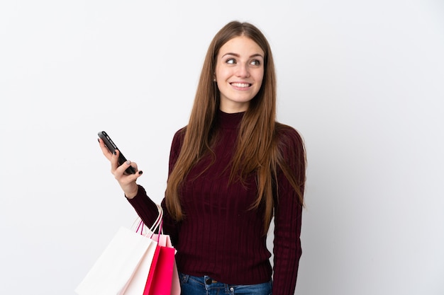 Mujer joven sobre pared blanca aislada con bolsas de compras y un teléfono móvil