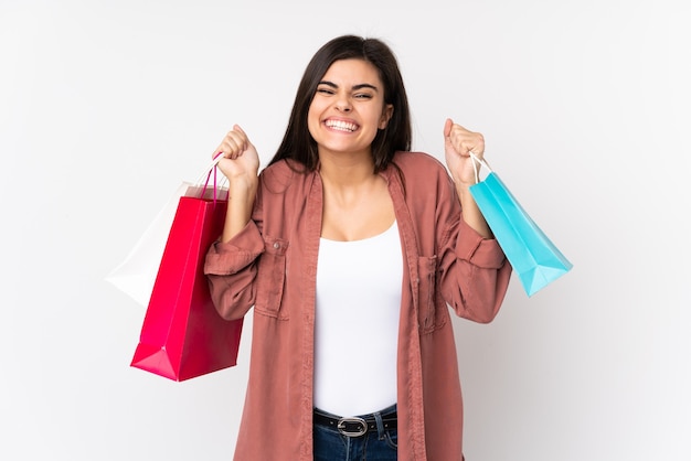 Mujer joven sobre pared blanca aislada sosteniendo bolsas de compras y sonriendo