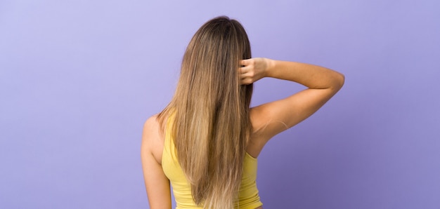 Mujer joven sobre pared púrpura aislada en posición trasera y pensando