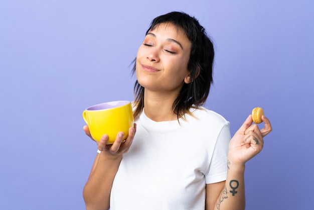 Mujer joven sobre pared púrpura con coloridos macarons franceses y una taza de leche