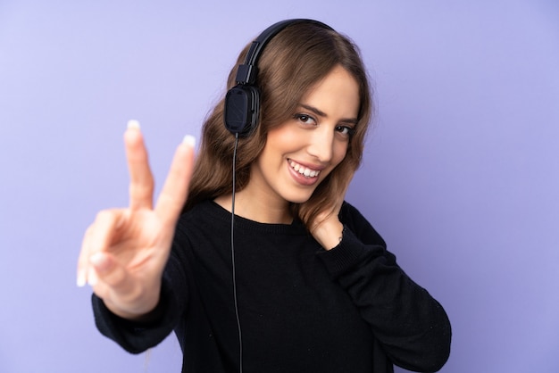 Mujer joven sobre pared púrpura escuchando música y cantando