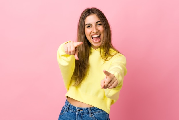 Mujer joven sobre pared rosa aislada sorprendida y apuntando al frente