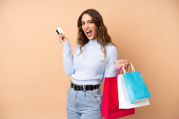 Mujer joven sobre pared sosteniendo bolsas de compra y una tarjeta de crédito
