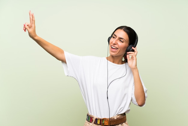 Mujer joven sobre pared verde aislada escuchando música con auriculares