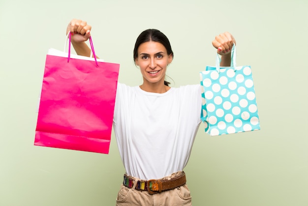 Mujer joven sobre la pared verde aislada que sostiene muchas bolsas de compras