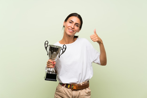 Mujer joven sobre la pared verde aislada que sostiene un trofeo