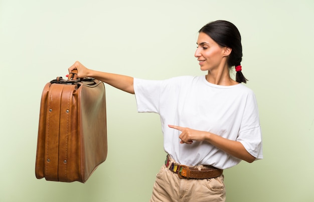 Mujer joven sobre pared verde aislada sosteniendo un maletín vintage