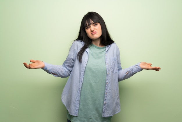 Foto mujer joven sobre pared verde infeliz y frustrada con algo porque no entiende algo