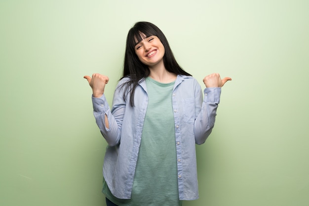 Mujer joven sobre la pared verde que da un pulgar hacia arriba gesto con ambas manos y sonriendo