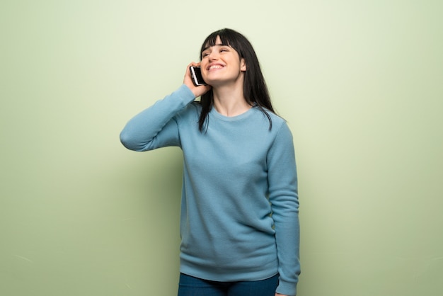 Mujer joven sobre la pared verde que mantiene una conversación con el teléfono móvil