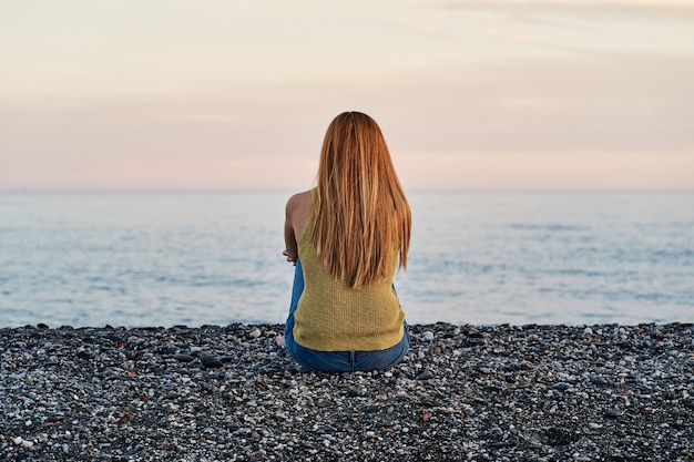 Foto mujer joven sola sentada en la arena de la playa al atardecer. concepto de relajación y meditación.