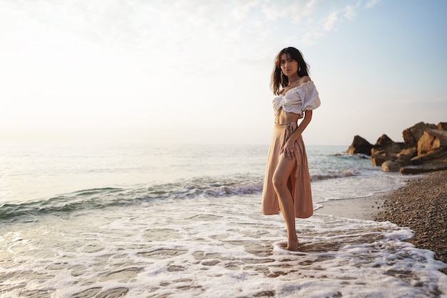 Mujer joven solitaria camina por la orilla del mar al atardecer