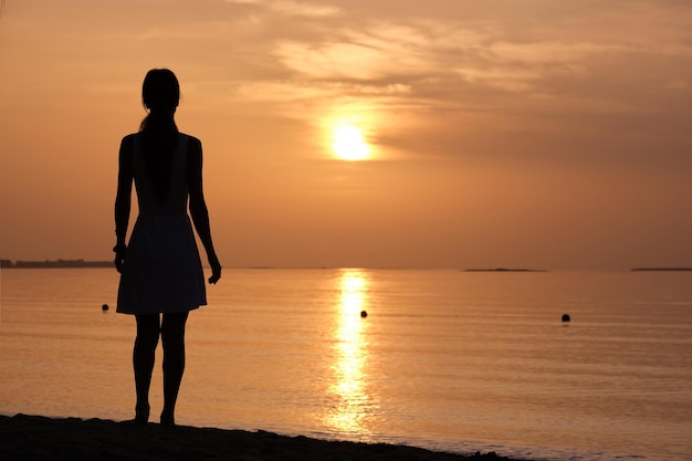 Mujer joven solitaria de pie en la playa del océano junto al mar disfrutando de una cálida noche tropical