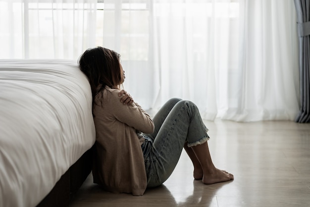 Mujer joven solitaria que se siente deprimida y estresada sentada en el dormitorio oscuro, emoción negativa y concepto de salud mental