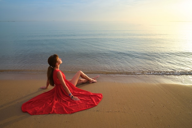 Mujer joven solitaria sentada en la playa de arena del océano junto al mar disfrutando de una cálida noche tropical.