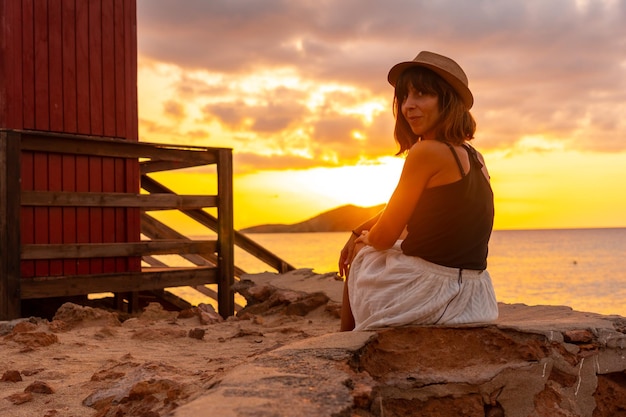 Mujer joven con sombrero al atardecer en la playa de Cala Comte en la isla de Ibiza Balearic