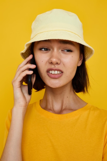 Mujer joven en un sombrero amarillo estilo juvenil casual hablando por teléfono aislado fondo