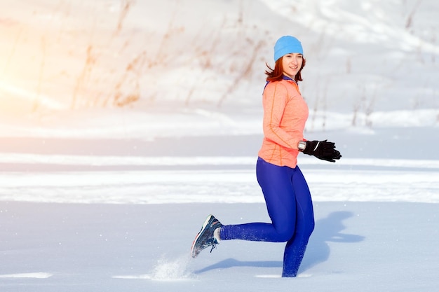 Una mujer joven con un sombrero azul brillante un suéter naranja y faldas de alce corre a través de la nieve de invierno