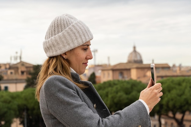 Una mujer joven con sombrero blanco tomando una foto con su teléfono móvil en Roma Italia