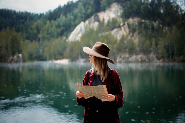 Mujer joven con sombrero y camisa roja con mapa cerca del lago