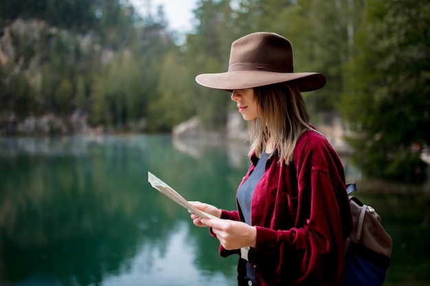 Mujer joven con sombrero y camisa roja con mapa cerca del lago