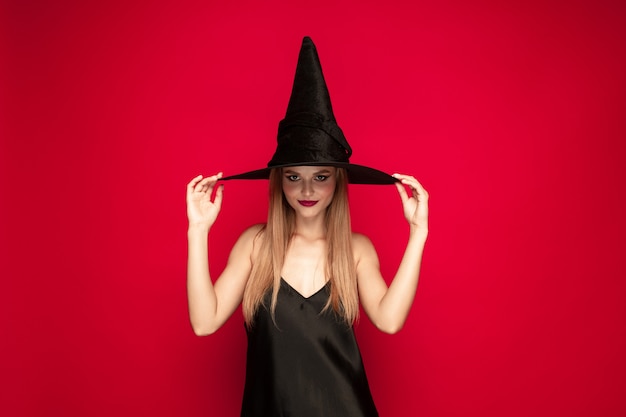 Mujer joven con sombrero como bruja sobre fondo rojo.