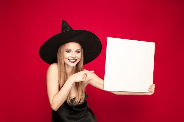 Mujer joven con sombrero como bruja sobre fondo rojo.