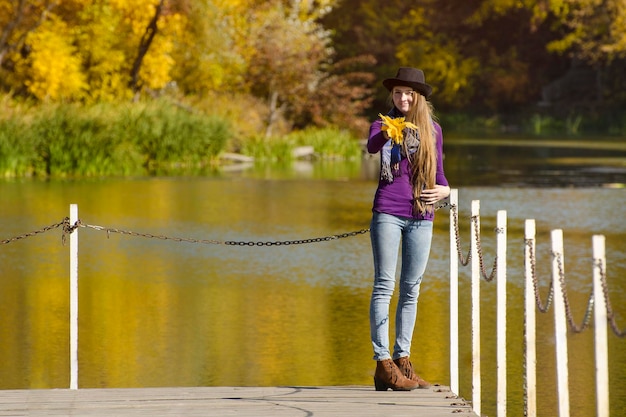 Mujer joven en el sombrero está de pie en el muelle Día soleado de otoño Vista posterior