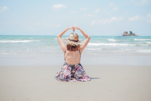 Una mujer joven con sombrero está sentada en la playa