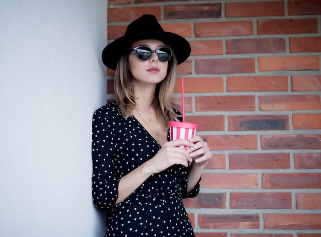 Mujer joven con sombrero y gafas de sol con una bebida