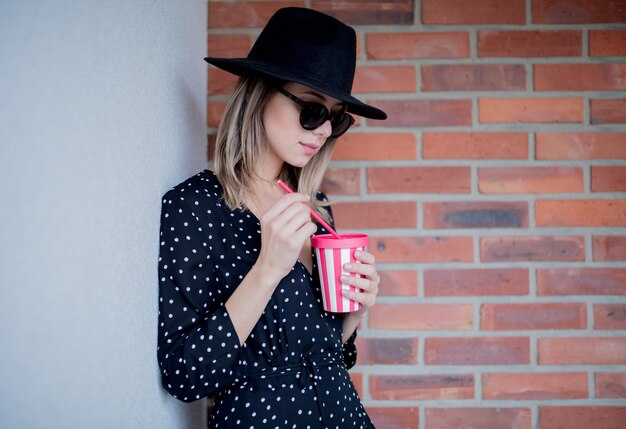 Mujer joven con sombrero y gafas de sol con una bebida