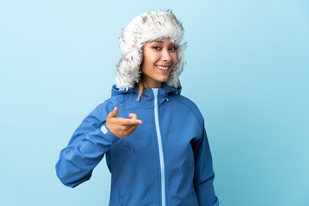 Mujer joven con sombrero de invierno aislado en el espacio azul señala con el dedo