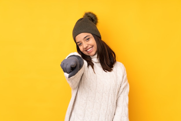 Mujer joven con sombrero de invierno sobre amarillo aislado le señala con el dedo con una expresión de confianza